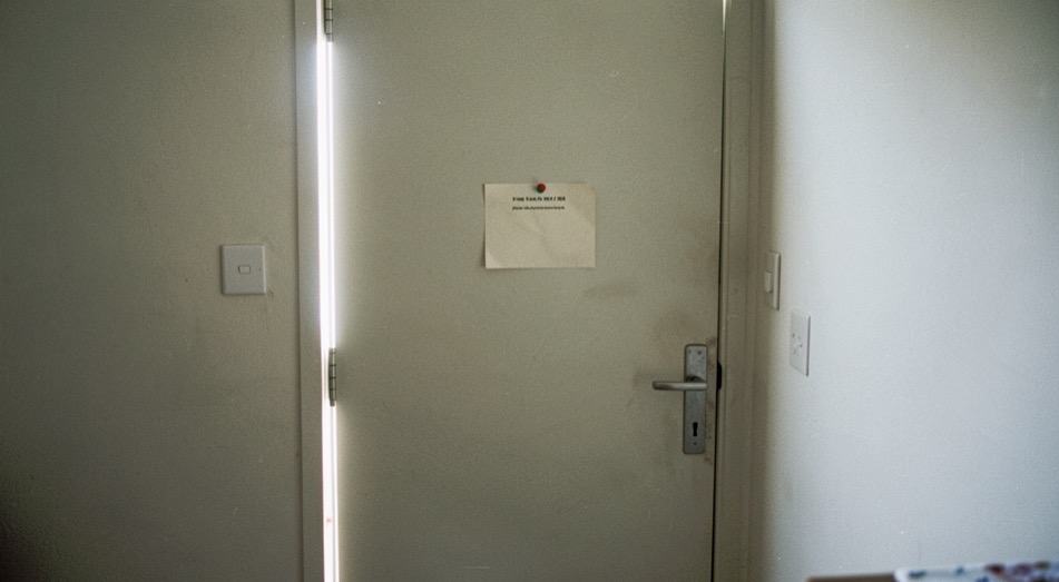 A plain closed door of a back room with a small paper notice pinned at eye level and daylight under the door